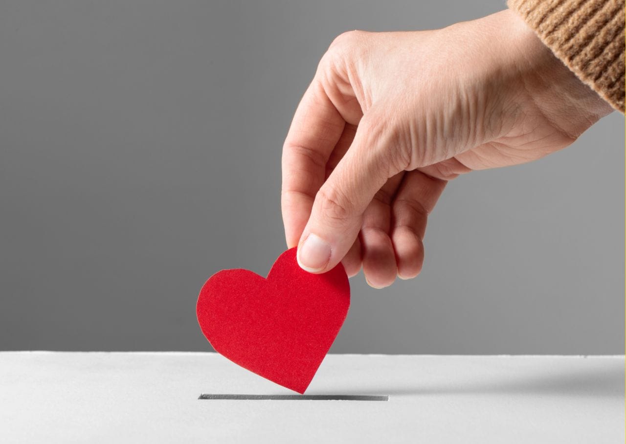 Success Stories 1 A hand delicately places a red paper heart into a slot on a gray surface, symbolizing the passion infused in civil engineering projects even when outsourcing is involved.