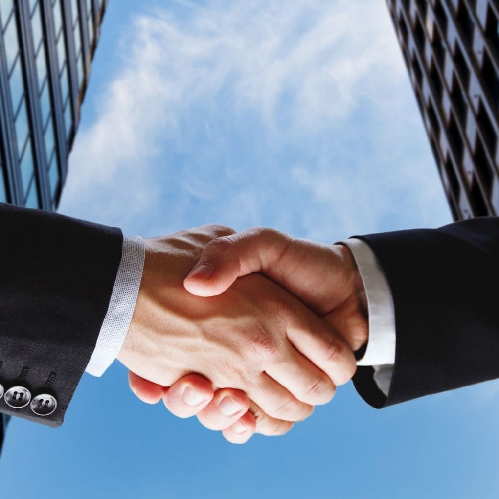 Keltic Engineering's Seamless Synergy with AXA Engineers - A Chronicle of Innovation and Partnership 6 Two individuals from Keltic Engineering shake hands against a backdrop of skyscrapers and a blue sky with clouds. Both wear dark suits, emphasizing a professional setting that symbolizes innovation and partnership.