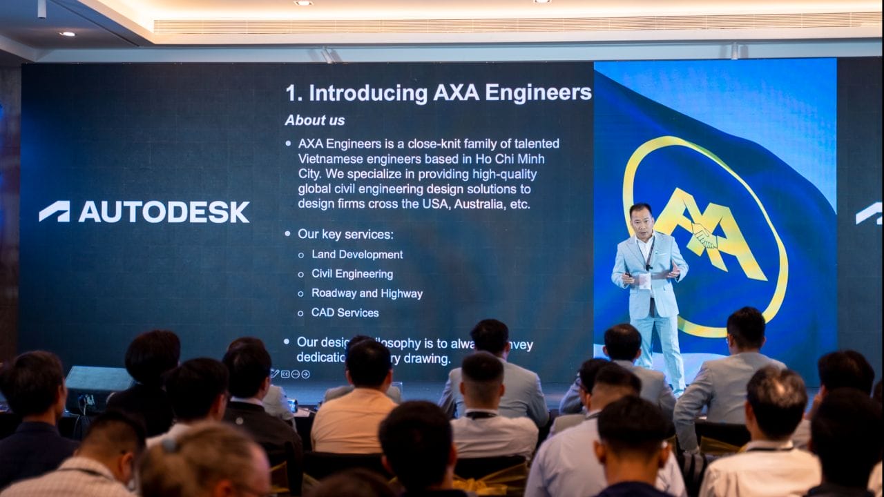 A speaker presents in front of an audience at a conference. The slide on the screen is titled 1. Introducing AXA Engineers, detailing their civil engineering outsourcing services. The logo of Autodesk is visible on the left side of the screen.