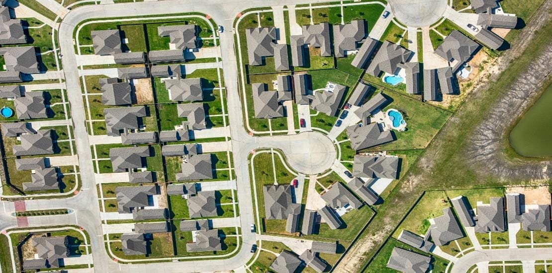 Aerial view of a suburban neighborhood with neatly arranged houses, green lawns, roads, and a cul-de-sac. A few homes boast pools in their backyards. This orderly community exemplifies how outsourcing land development services can create harmonious blends of straight and curved streets with uniform housing layouts.