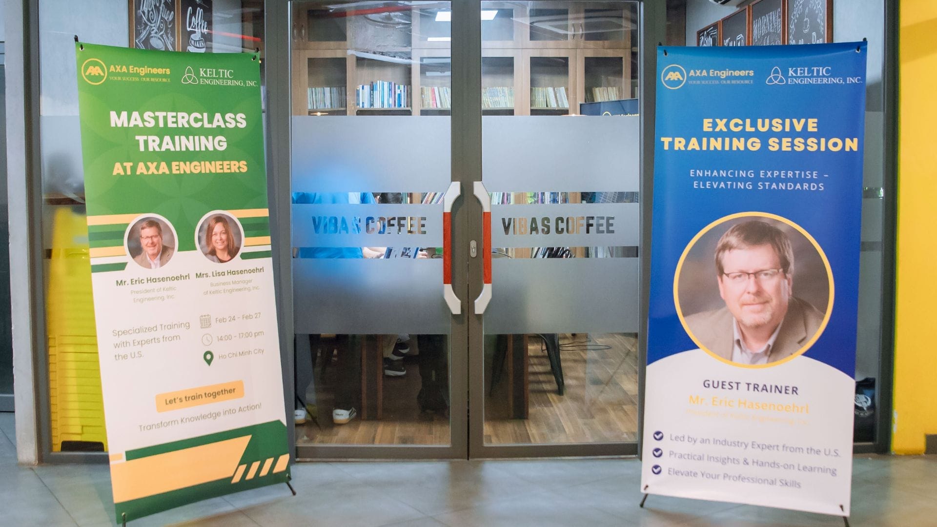 Two vertical banners stand in front of glass doors labeled Vidas Coffee. The left banner promotes a masterclass training with images of two people, highlighting a PE Certification opportunity. The right banner advertises an exclusive training session featuring AXA Engineers with an image of one person.