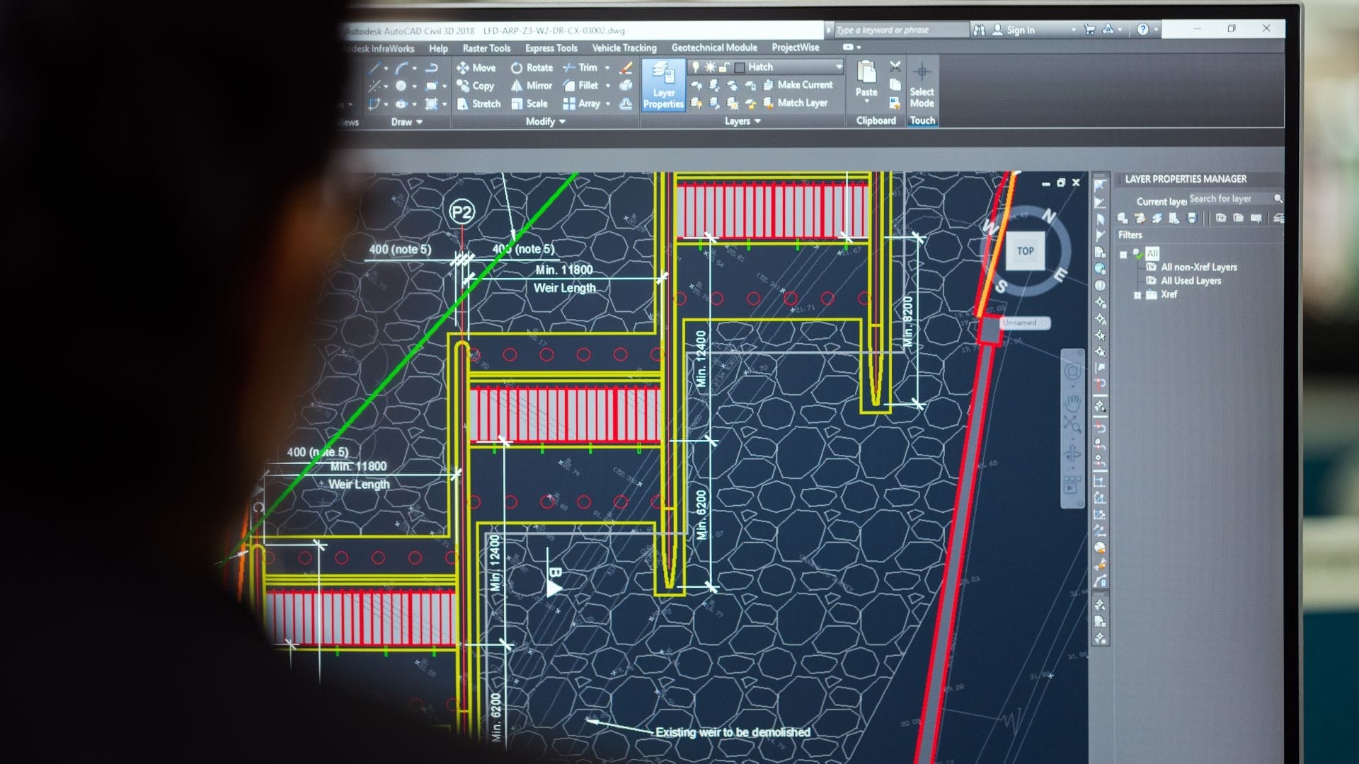 Civil Engineering Outsourcing A person is viewing a computer screen displaying a detailed architectural design in AutoCAD, carefully considering the risks involved with civil engineering outsourcing—evident through precise lines, measurements, and colored highlights set against a dark grid background.