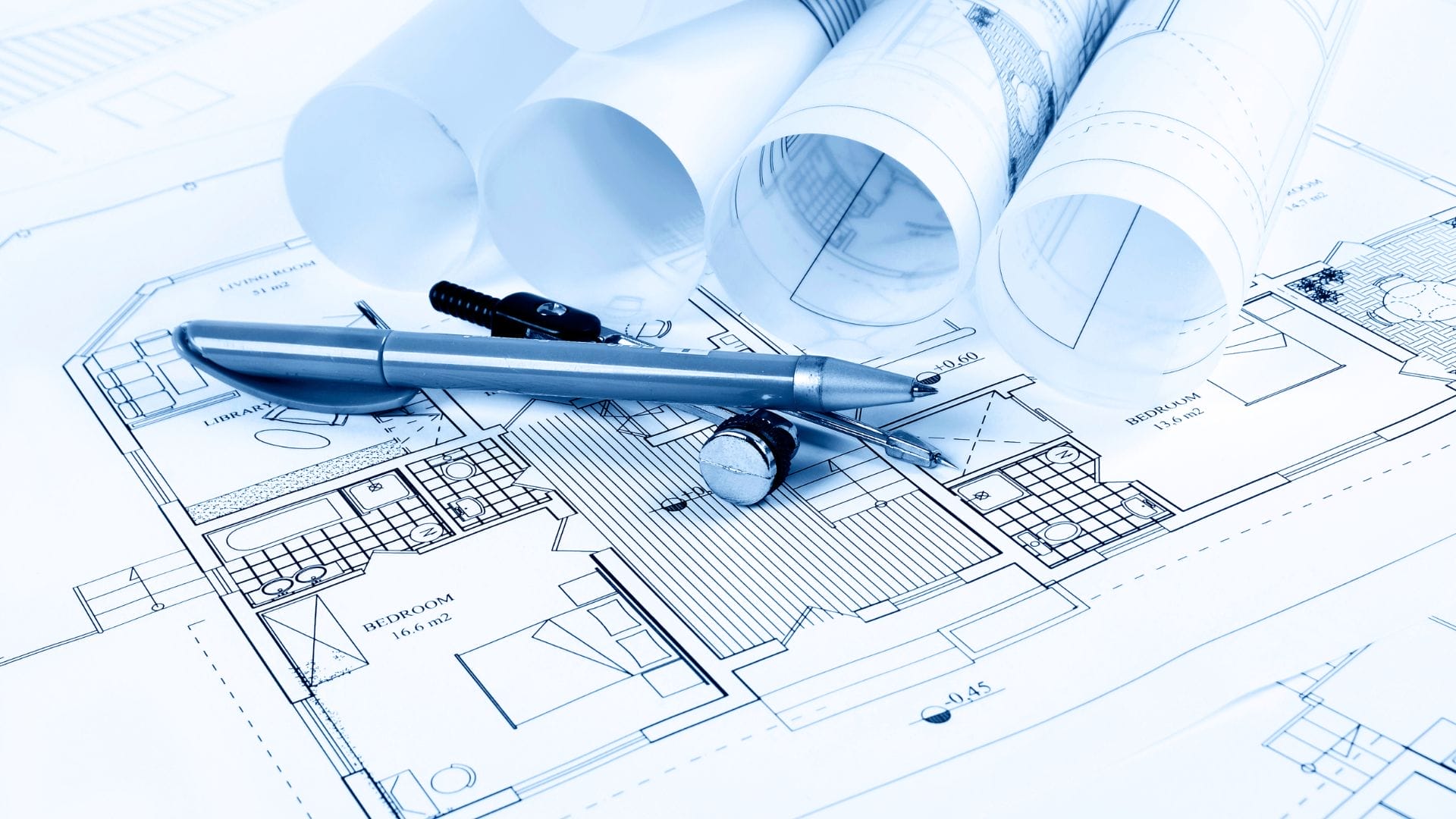 A collection of architectural blueprints lies on a table, overlaid with a silver pen, screws, and a small compass, evoking the precision required in civil engineering projects. The focus is on intricate floor plans and rolled-up documents awaiting decisions under tight deadlines.