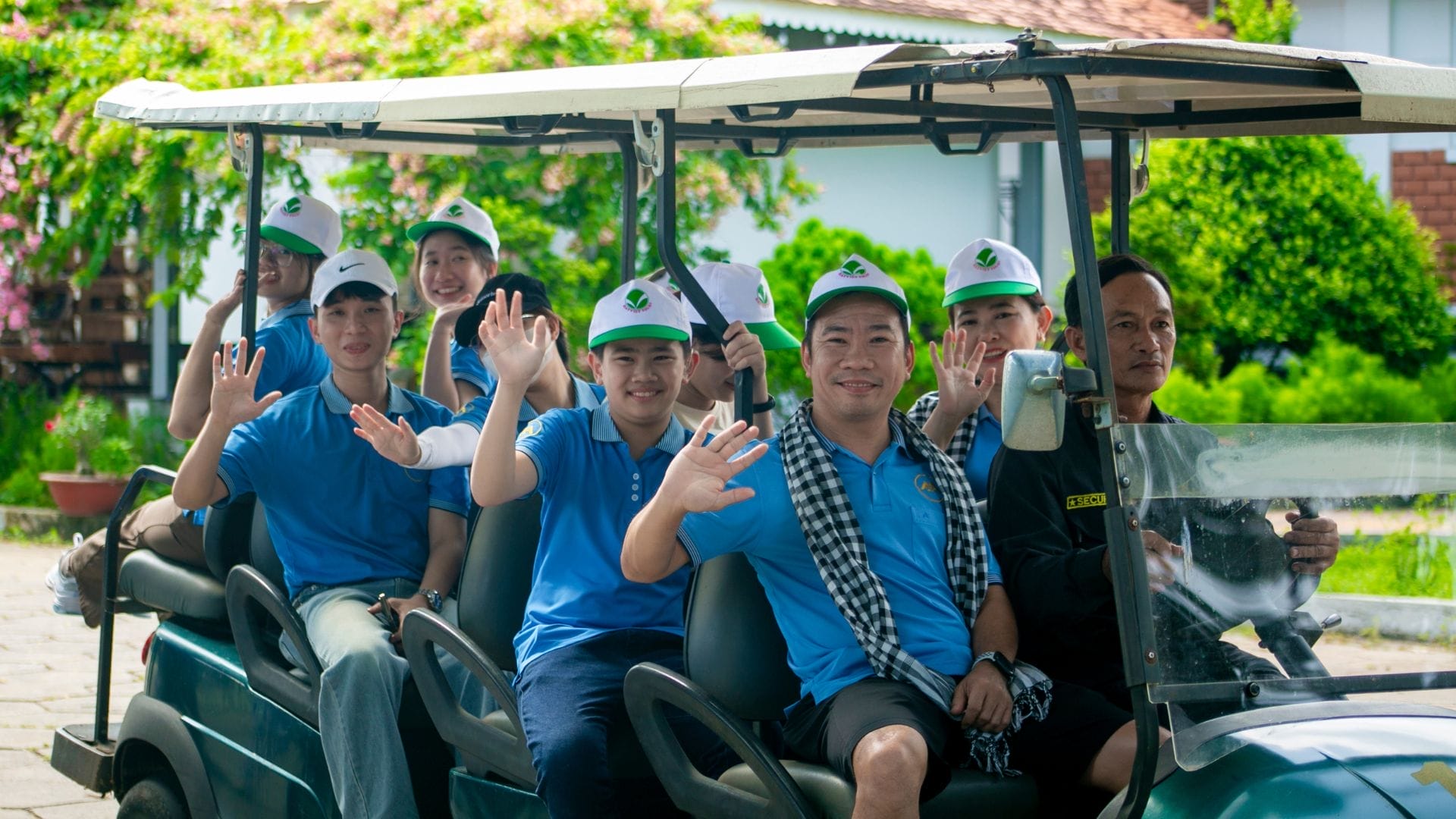 Civil Engineering Outsourcing A group of people wearing blue shirts and white caps sit in a golf cart, smiling and waving at the camera as they enjoy meaningful moments together at the KELTIC–AXA Engineers Trip 2025 on a sunny day—highlighting the camaraderie that drives successful civil engineering outsourcing projects.