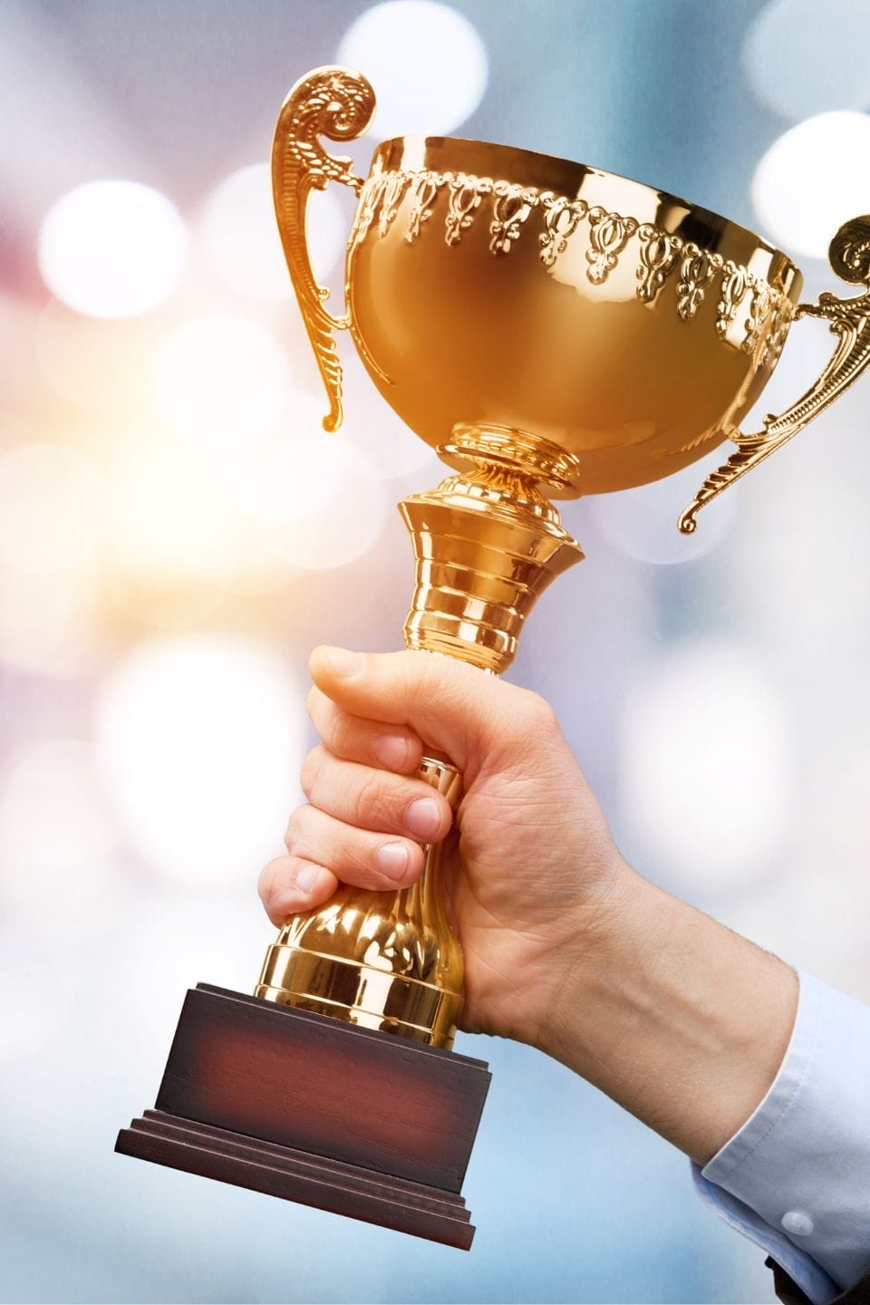 Civil Engineering Outsourcing A hand raises a gold trophy cup with ornate handles and a wooden base, symbolizing civil engineering outsourcing excellence.