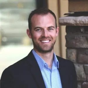 Civil Engineering Outsourcing A man with short brown hair and a trimmed beard, smiling in a blue shirt and dark blazer, stands by a stone wall; civil engineering outsourcing is referenced.