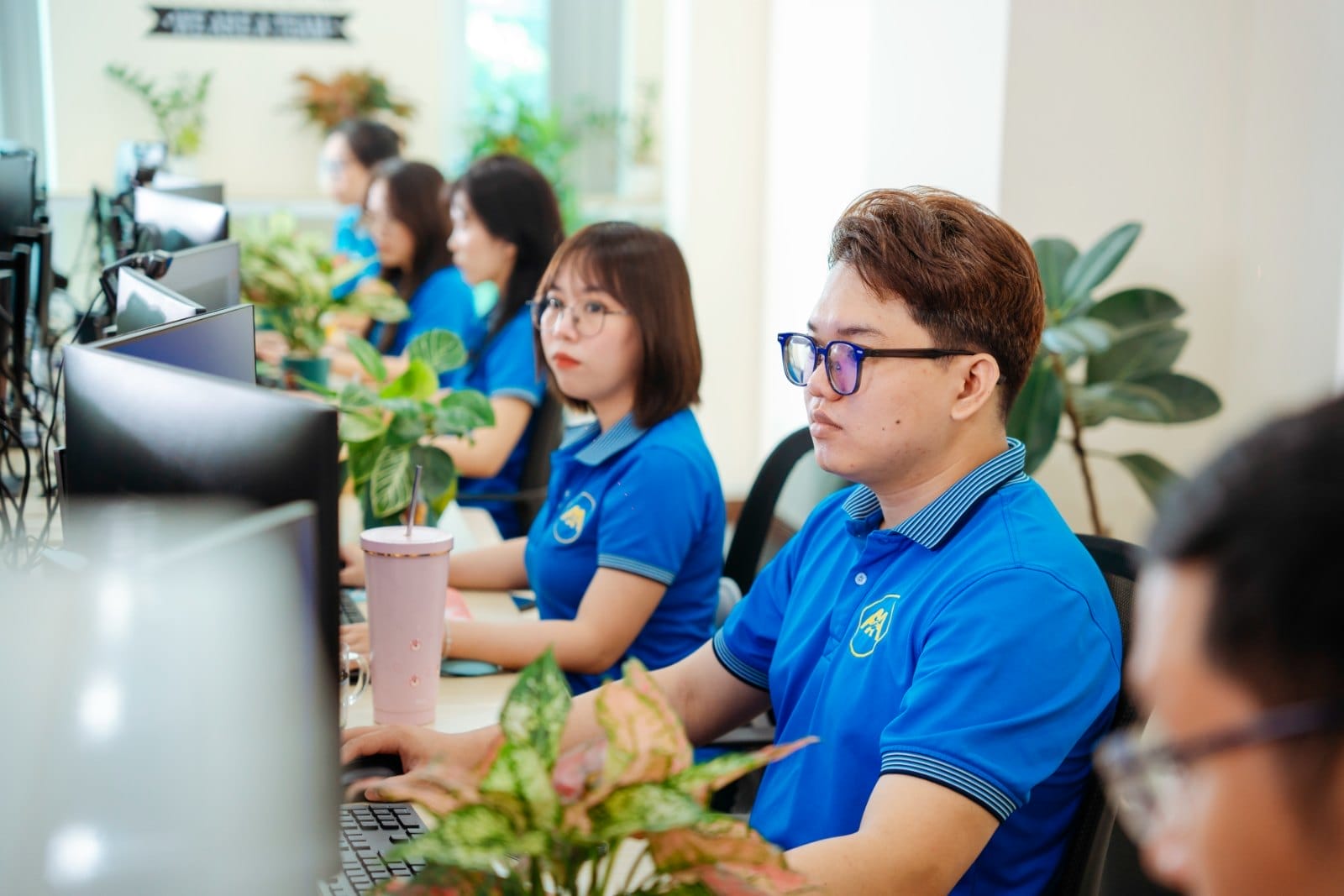 Civil Engineering Outsourcing A team in blue uniforms works at computers in a bright office, showcasing civil engineering outsourcing by AXA Engineers.