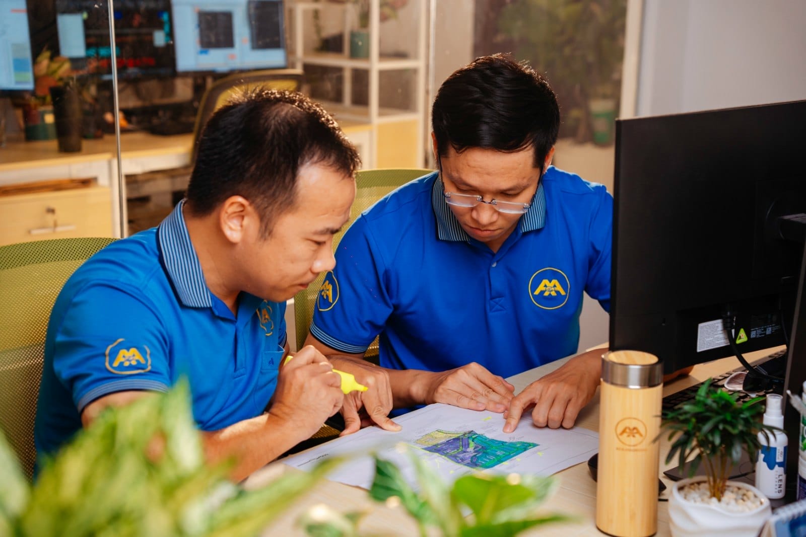 Civil Engineering Outsourcing Two men in blue shirts sit at a desk in an AXA Engineers office, reviewing plans during a civil engineering outsourcing meeting.