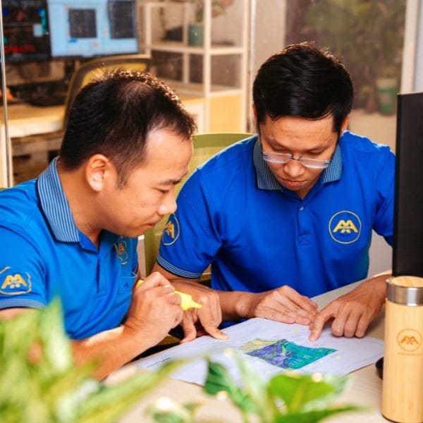 Our Risk-Free Pilot Project 9 Civil Engineering Outsourcing Two men in matching blue shirts sit at a desk, reviewing civil engineering outsourcing plans. Office supplies and plants surround them.