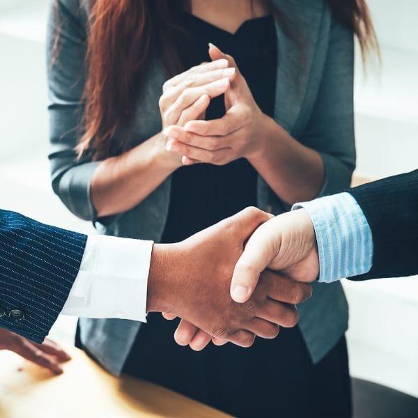 Civil Engineering Outsourcing Two people in business attire shake hands as a woman nearby applauds, symbolizing successful civil engineering outsourcing teamwork.