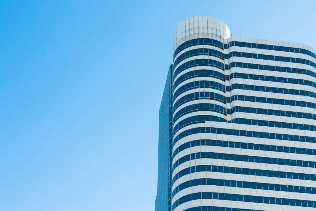 Civil Engineering Outsourcing A modern high-rise with rounded corners and white stripes, reflecting innovative civil engineering outsourcing, rises against a blue sky.