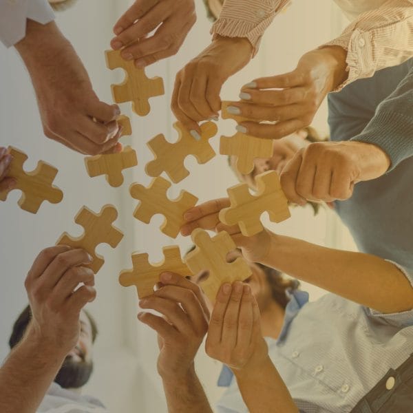 Civil Engineering Outsourcing A team engaged in civil engineering outsourcing stands in a circle, each holding a wooden puzzle piece, collaborating to connect them.