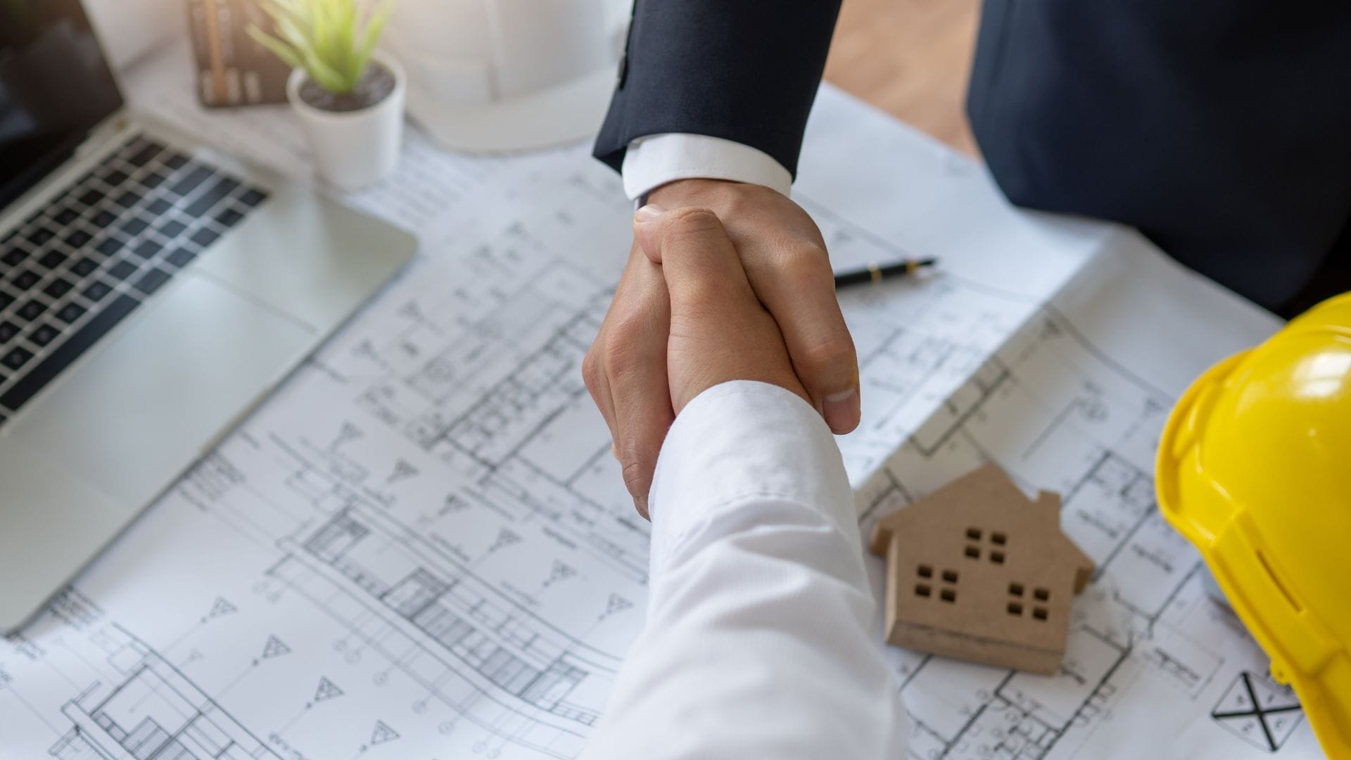 Civil Engineering Outsourcing Two people shaking hands over a table with blueprints and a laptop, symbolizing civil engineering outsourcing partnership.