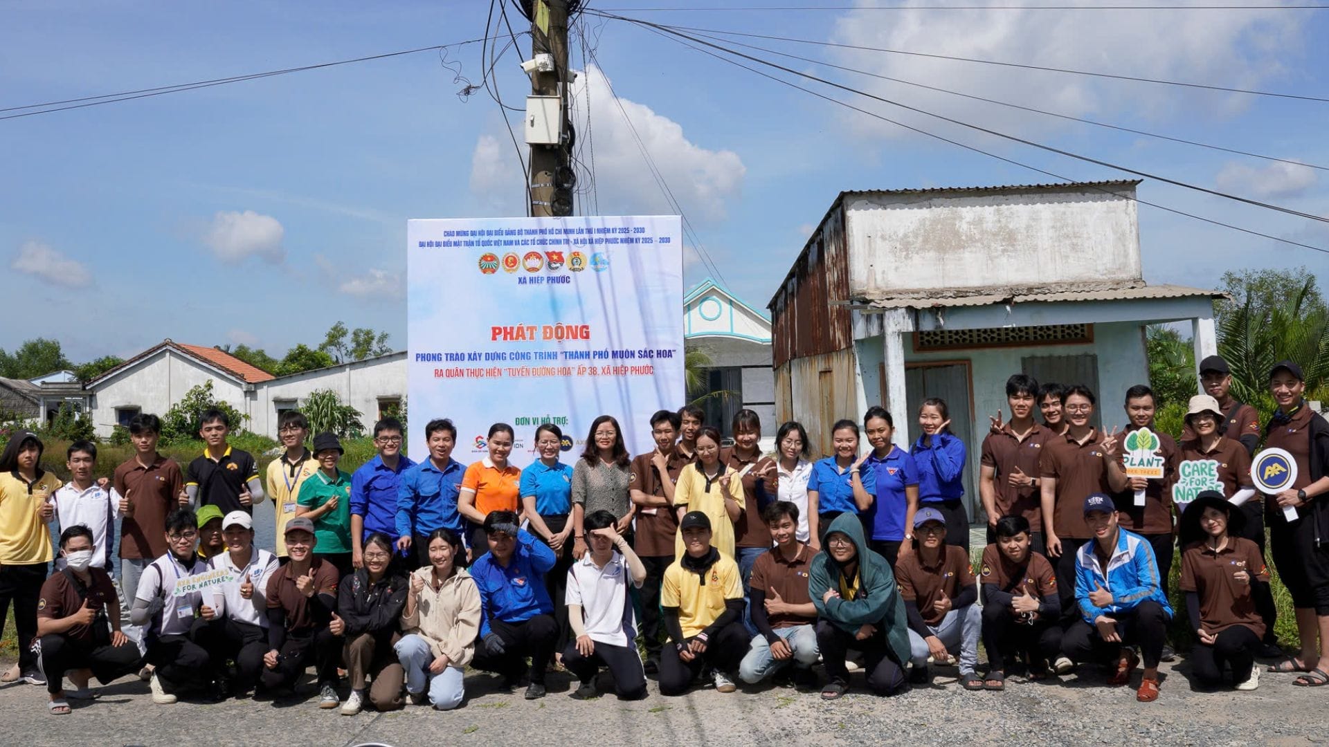 Civil Engineering Outsourcing A group in uniforms smiles before a banner on a rural street, marking phase 1 of civil engineering outsourcing under blue skies.
