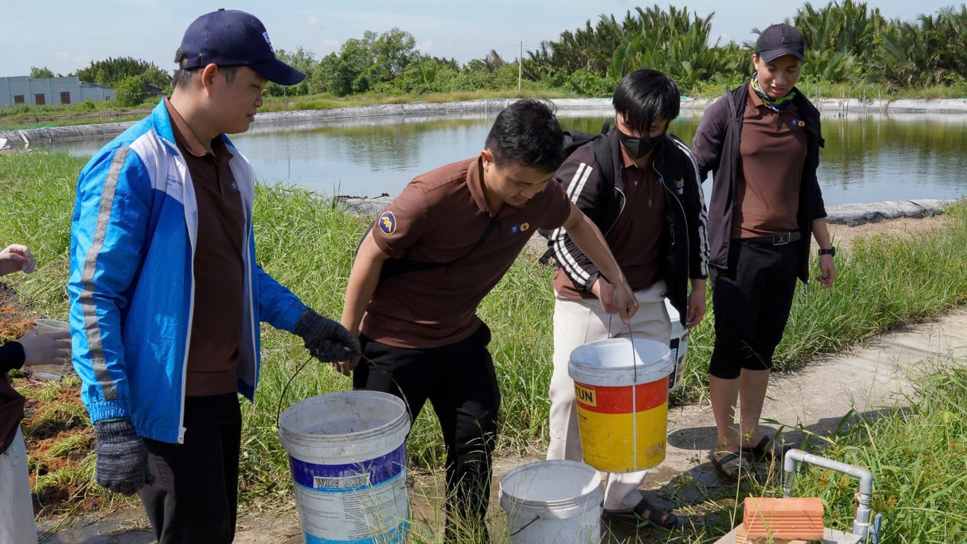 Civil Engineering Outsourcing Four people by a pond collect water samples in buckets, representing phase 1 of a sustainable civil engineering outsourcing project.