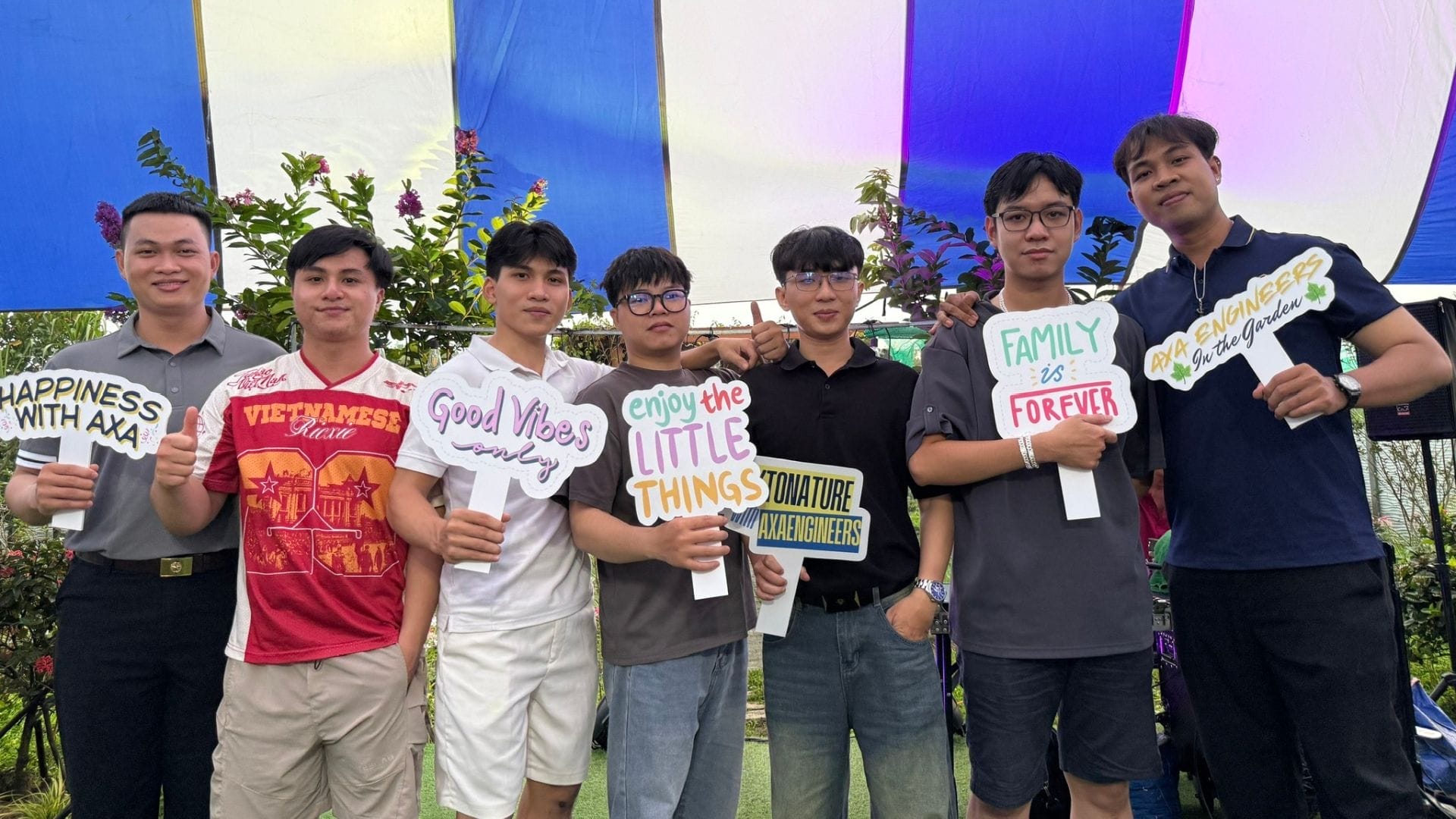 Civil Engineering Outsourcing Seven young men under a striped tent on their Garden Trip, holding signs with positive messages and civil engineering outsourcing slogans.