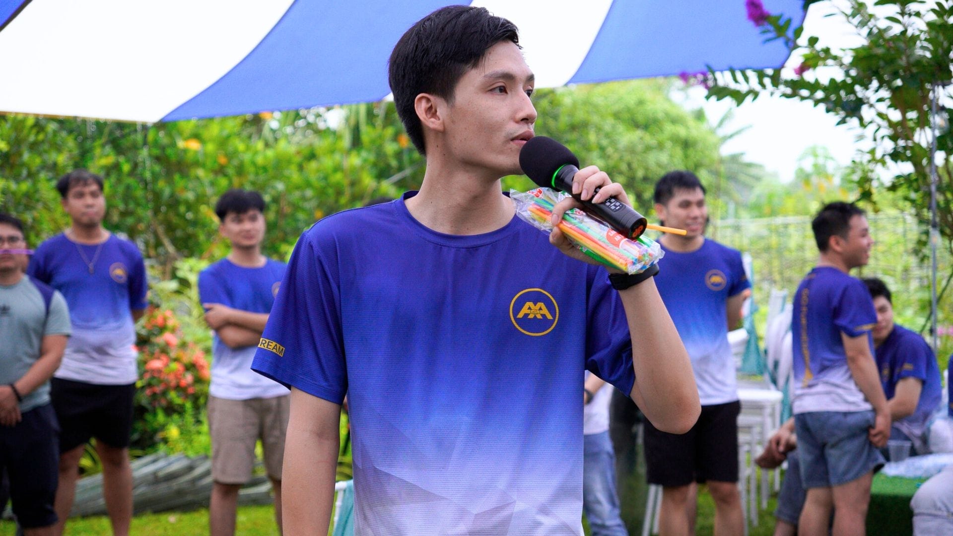 AXA Engineers Garden Trip – Where Happiness Finds Its Way Home 9 Civil Engineering Outsourcing A young man in a blue gradient shirt holds a microphone and water gun, celebrating civil engineering outsourcing at AXA Engineers Garden.