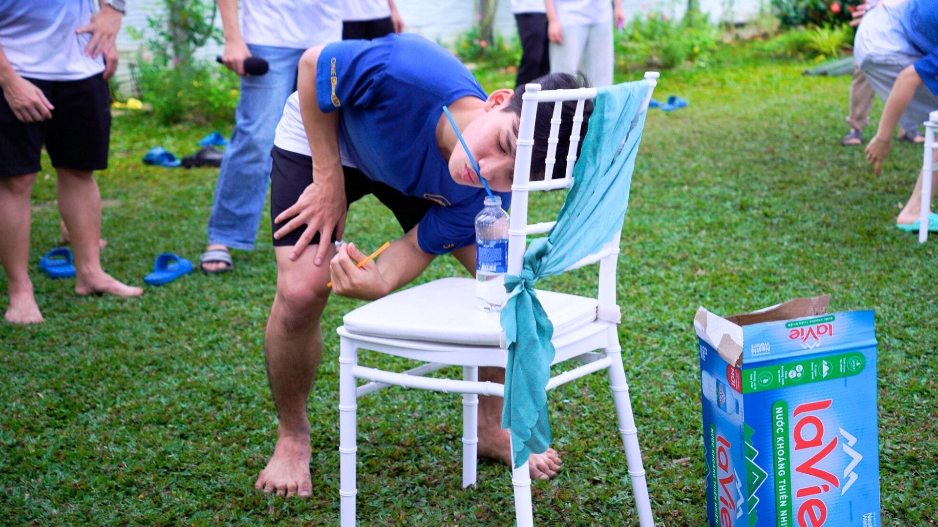 Civil Engineering Outsourcing During a civil engineering outsourcing event, a person in blue tries to pick up a bottle by mouth near others on grass chairs.