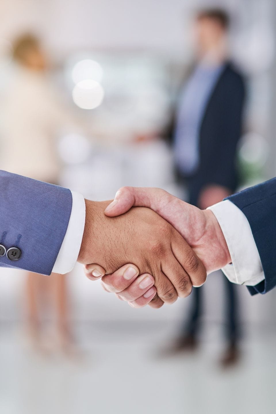 Our Risk-Free Pilot Project 1 Civil Engineering Outsourcing Close-up of two professionals in business attire shaking hands, with blurred colleagues behind, marking a civil engineering outsourcing deal.