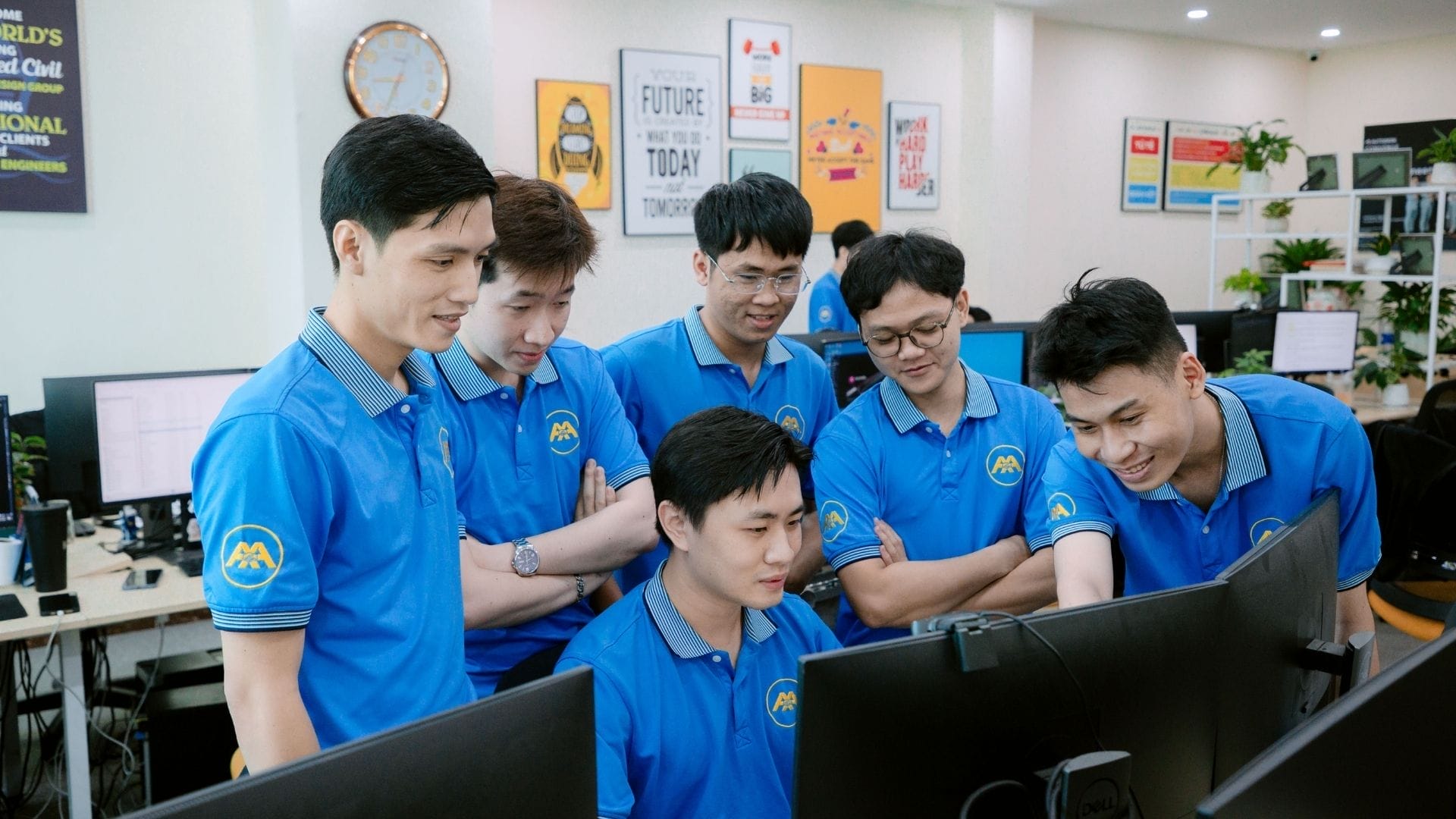 Civil Engineering Outsourcing Six AXA Engineers in blue shirts gather around monitors, representing civil engineering outsourcing in a vibrant, certified office.