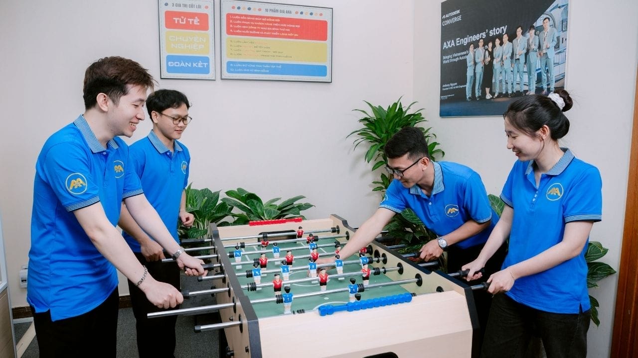 Civil Engineering Outsourcing Four AXA civil engineering outsourcing team members in blue shirts play foosball in a lively office, all smiling and engaged.
