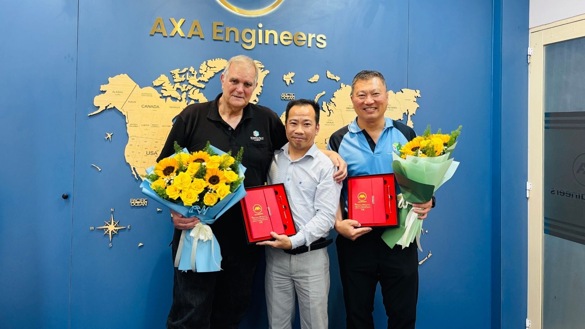 Civil Engineering Outsourcing Three men stand before a blue AXA Engineers wall, celebrating civil engineering outsourcing wins with 12D Solutions and holding awards.