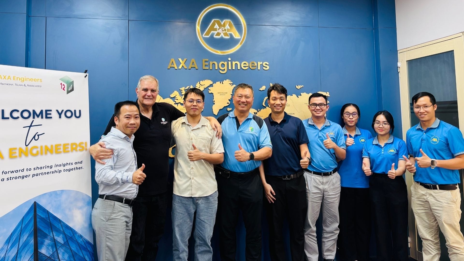 Civil Engineering Outsourcing Nine people in business casual pose with thumbs up before an AXA Engineers sign, celebrating civil engineering outsourcing success.
