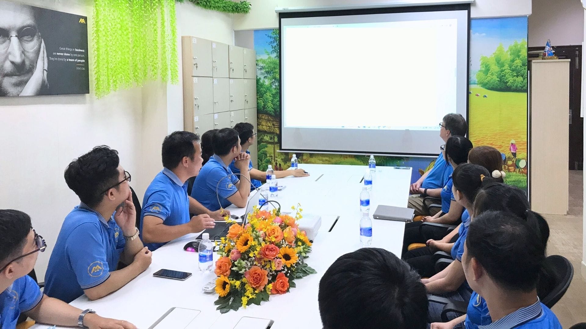 Civil Engineering Outsourcing A group in blue shirts sits around a conference table, watching a civil engineering outsourcing presentation in a bright meeting room.