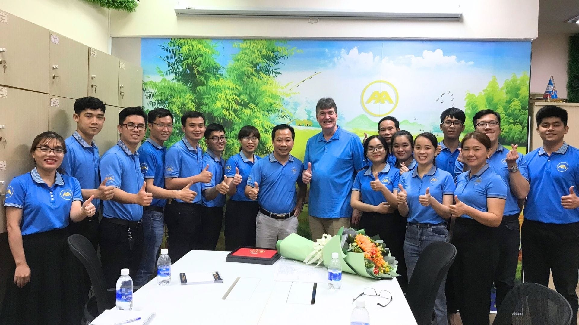 Civil Engineering Outsourcing A group in blue shirts stands together in a classroom for a civil engineering outsourcing event, smiling with flowers and documents on the table.