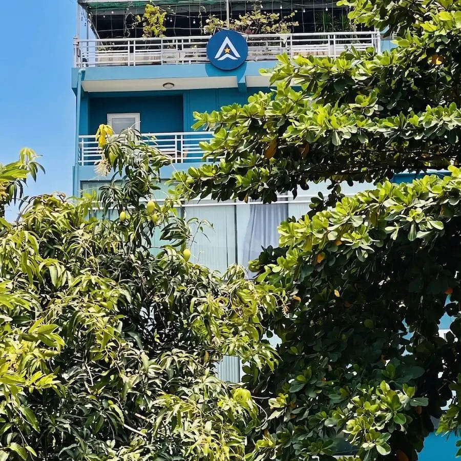 Civil Engineering Outsourcing A blue multi-story building behind green trees, with a white A sign, under clear skies. Ask AXA Engineers about civil engineering outsourcing.